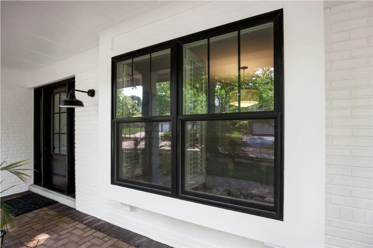 Two large black-framed double-hung windows on a white painted brick exterior with a covered front porch and black gooseneck light fixture.