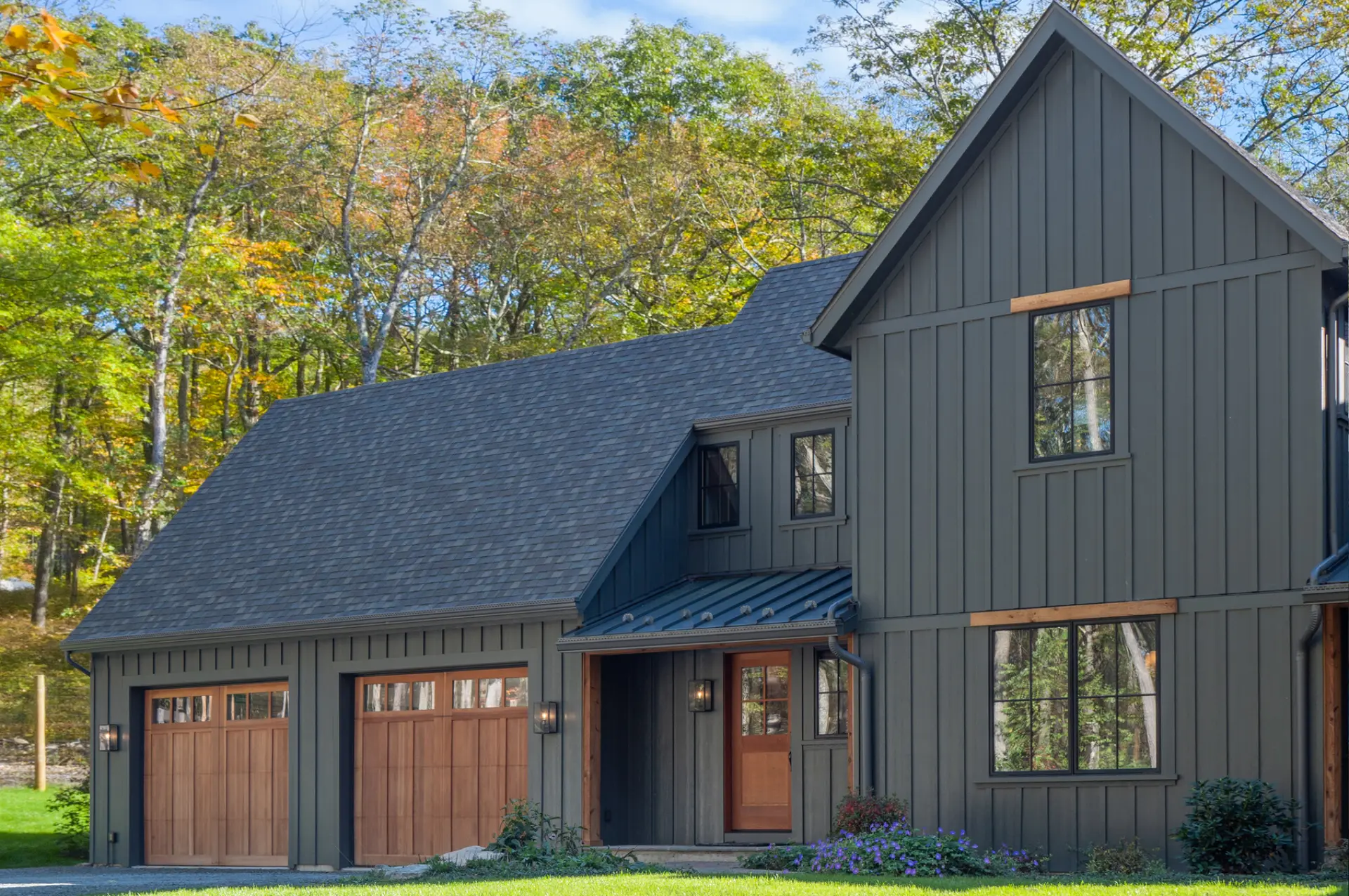 A two-story dark gray Hardie board-and-batten home with matching dark trim, natural wood garage doors, and a covered entry porch.