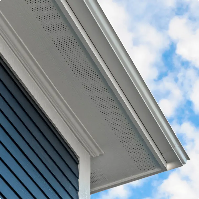 Close-up detail of a Hardie soffit and trim assembly in white meeting a dark Hardie lap siding wall, with a partly cloudy sky above.